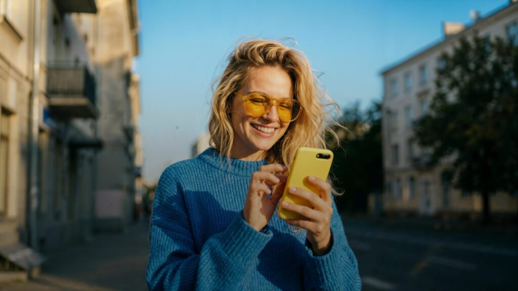 Person in lilafarbener Jacke bedient ein Smartphone vor einer Häuserzeile